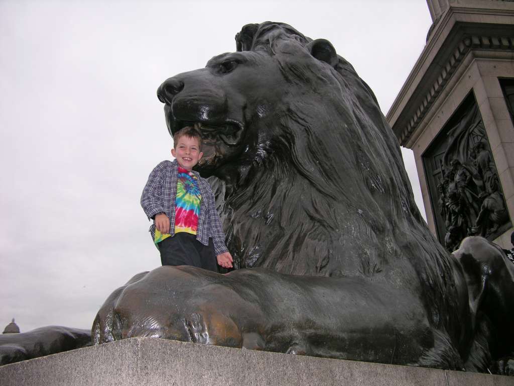 London 01 08 Trafalgar Square Nelson's Column is in the centre of Trafalgar Square, surrounded by fountains and four huge bronze lions. The column is topped by a statue of Lord Nelson, the admiral who commanded the British Fleet at Trafalgar (1805), a British naval victory of the Napoleonic Wars. This is a favourite resting place, to feed the pigeons, and to climb on to the statues. On the north side of the square is the National Gallery.